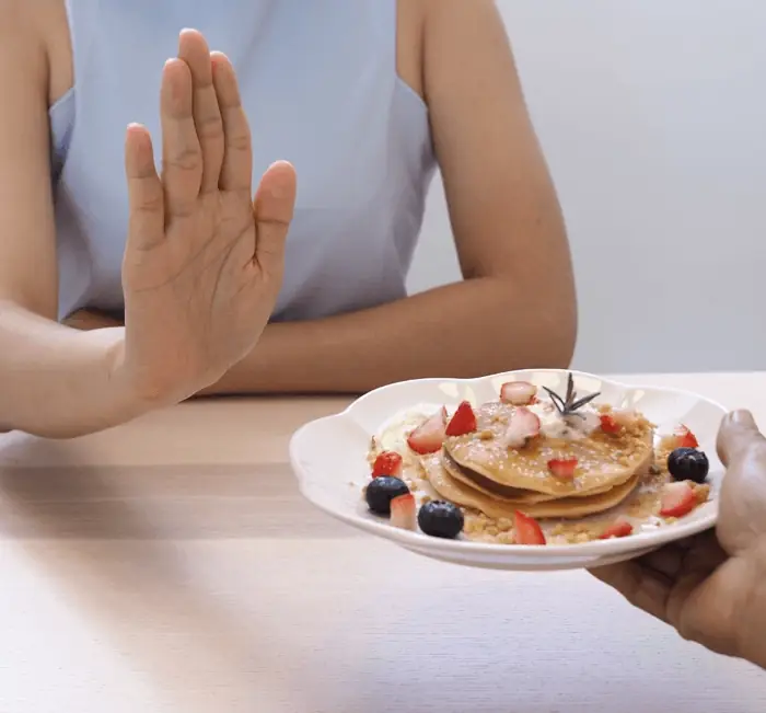 A hand raised to decline a plate of pancakes, illustrating appetite signalling