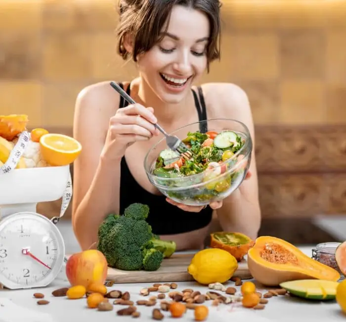 Someone eating a bowl of salad surrounded by fresh fruit and vegetables